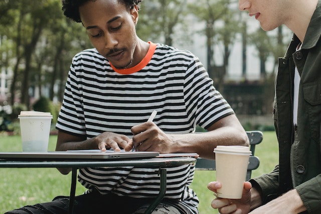 Two tenants sit together and one tenant in a black and while striped shirt writes notice to their landlord indicating they want to break their lease as they need to relocate for school